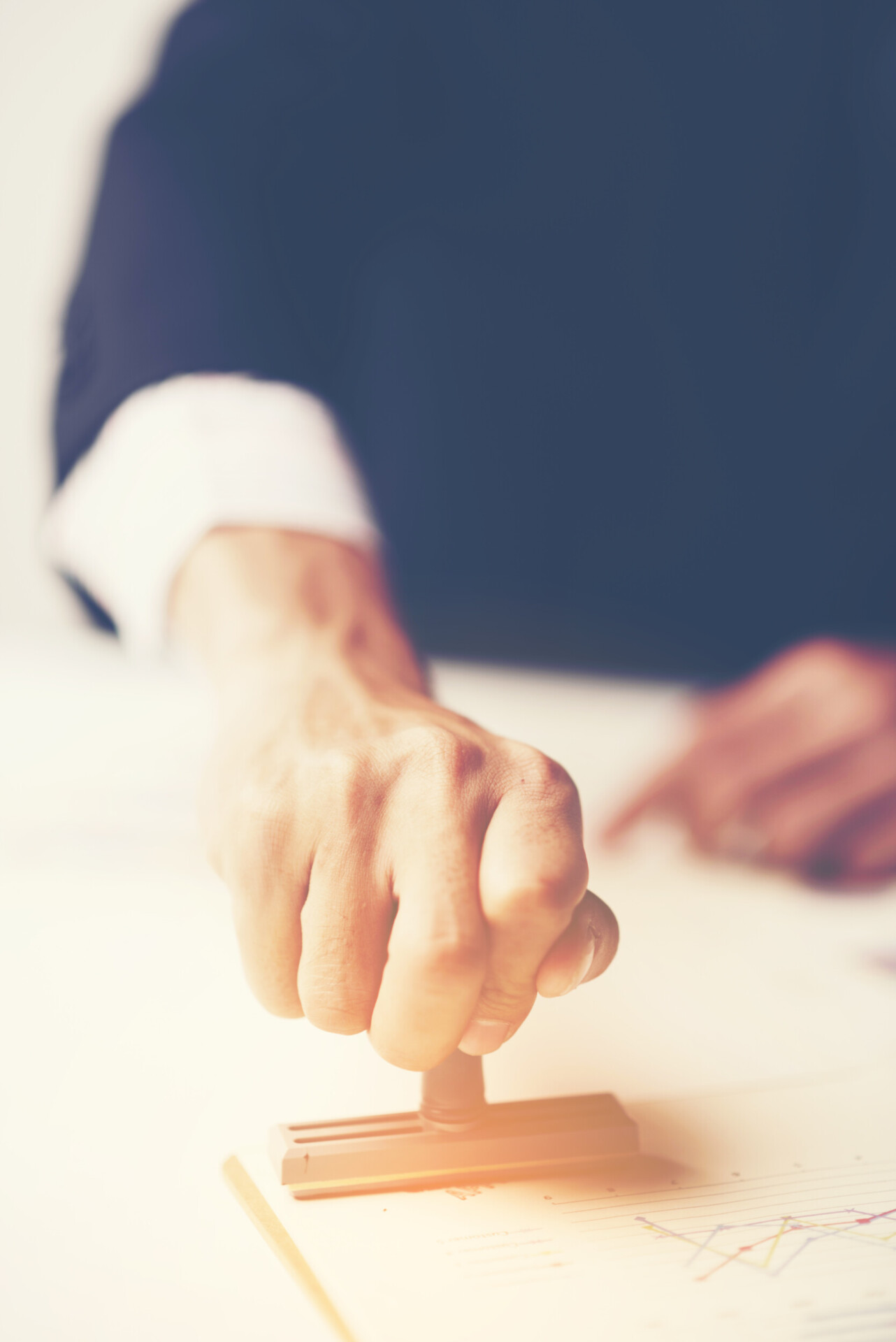 close up of a person's hand stamping with approved stamp on document at desk